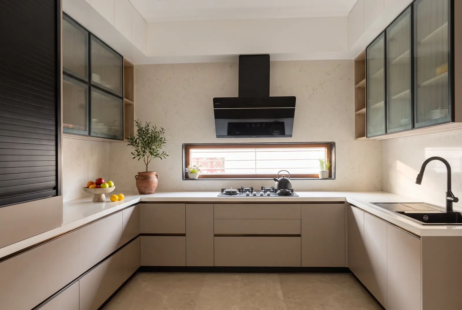 A U-shaped kitchen in cashmere-grey matt with fluted-glass wall cabinets and a long window above the hob.