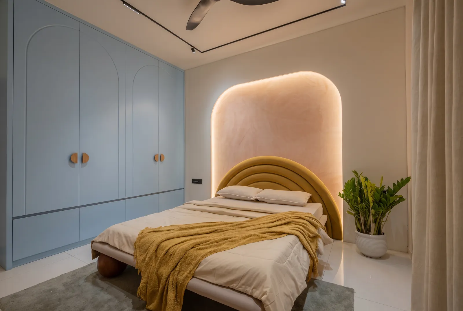 A children's room with pale blue matt wardrobes, a mustard headboard and a softly lit terracotta arch.